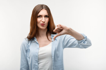 Beautiful girl in casual clothes holding thumb down. Concept of dislike. Studio shot, white background