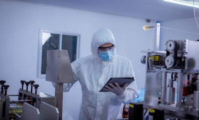 Technician worker wearing protective suite , glove are inspect machine with check  face mask manufacturing process to safe and against from virus.