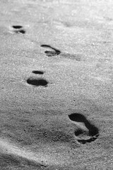 Black and white close-up picture of footprints on wet sand. Barefoot female footsteps on seashore. Travel bright contrast photo