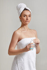 woman in bath towel holds tonic to remove makeup. skin cleansing