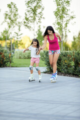 Young mother and her little daughter rollerskating in summer park