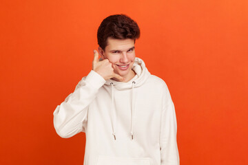 Call me. Self confident handsome young man in stylish sweatshirt holding fingers near ear,...