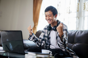 Asian student exciting in fron of laptop to hearing a good news or pass the test at home. - obrazy, fototapety, plakaty