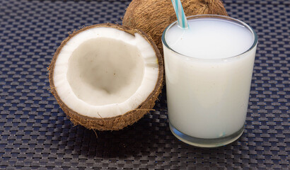 Half coconut and glass with coconut water on black surface