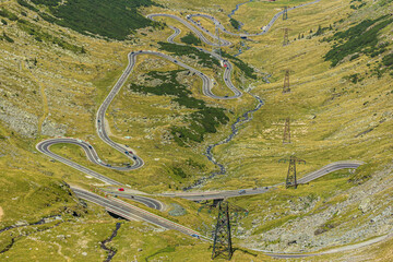 A mountain road.  The Transfagarasan (Transfăgărășan) road curls like a ribbon and intertwines with The Balea (B&acirc;lea) river along stright high-voltage power line.