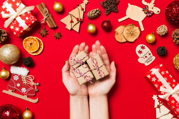 Top view of female hands holding a Christmas present on festive red background. Holiday decorations. New Year holiday concept