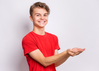 Portrait of cute smiling teen boy holding nothing - side view. Happy teenager with empty palms up - profile, over grey background. Child stretched out his hands - sign of begging or giving. - 379322123
