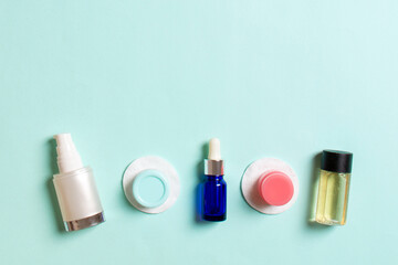 Top view of means for face care: bottles and jars of tonic, micellar cleansing water, cream, cotton pads on colored background. Bodycare concept with empty cpace for your ideas