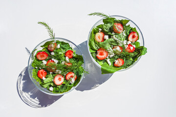Summer vegetables salad with fresh strawberries, basil, mozzarella and edible flowers in glass salad-bowls in garden at sunny day. Healthy eating. Organic and vegetarian food