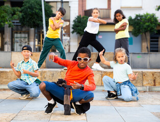 Obraz premium Positive girls and boys training hip hop on city street, outdoor dance class for kids