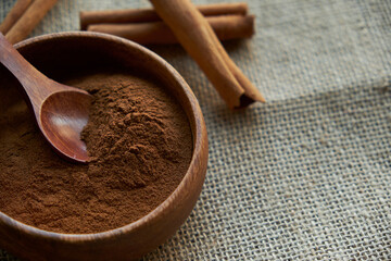 cinnamon sticks, tied with jute rope in rustic style. Ground cinnamon in a wooden bowl and vintage scoop. Close up on a black background. copy space for text. side view, flat lay.
