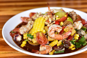 Thai Food. Green Papaya Salad (SOM-TUM) or Thai Style spicy seafood salad with shrimps, crab, Scallop, squid in a white plate on a wooden table.