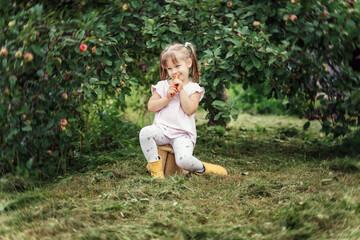 little girl eating carrots sitting under an apple tree in the country