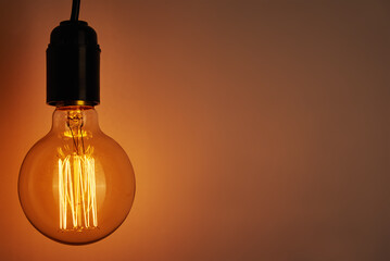Vintage light bulb on orange background, copy space. Glowing edison bulb
