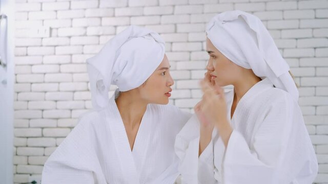 Two Asian girls in white bathrobes with towels on heads talking in living room.