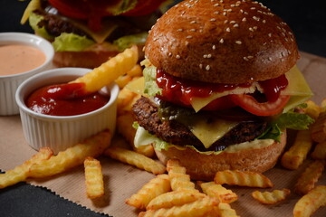 Homemade burger with grilled beef, cheese, onion, tomato, and green salad, sauce, with pickles and French fries