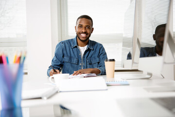 Naklejka na ściany i meble Happy african american creative businessman smiling while looking at camera in office