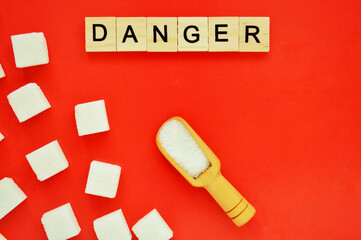 Refined sugar and wooden spoon with loose sugar on red background. Word danger of wooden blocks with letters