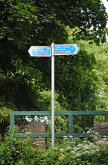 Rural Sign Post with Metal Pole & Directions beside Wooden Fence & Trees 