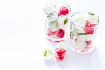 Cocktail glasses with berries in ice cubes on white table copy space