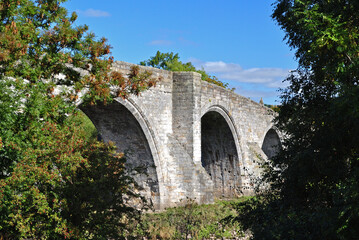Fototapeta na wymiar Ancient Stone River Bridge with Arches against Blue Sky 