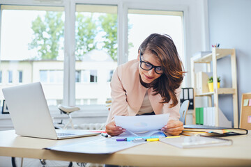 Busy woman working in small office reading documents