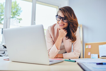 Smiling woman looking on laptop while working in small office or home office