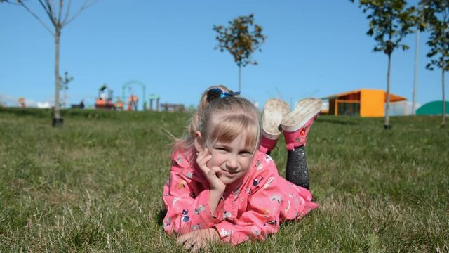 Beautiful little girl of six years old lies on the grass in the park and smiles