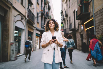 Naklejka premium Happy nifty woman using smartphone on street