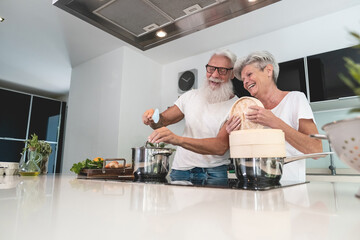 Senior couple cooking healthy meal at home in the kitchen - Elderly and joyful lifestyle - Focus on...