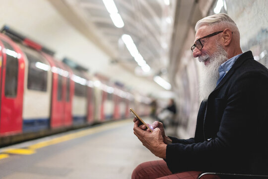 Hipster Senior Man Chatting On His Smartphone While Waits For Subway Train - Mature Man Having Fun With Technology Trends - Tech Elderly Joyful Night Concept - Focus On Face And Hand