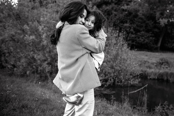 Stylish mother and daughter have fun outdoors in a field with green grass by the river when it rains