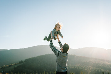 Portrait of a father holds, throws up happy daughter on hands walking on nature in autumn day. Dad...