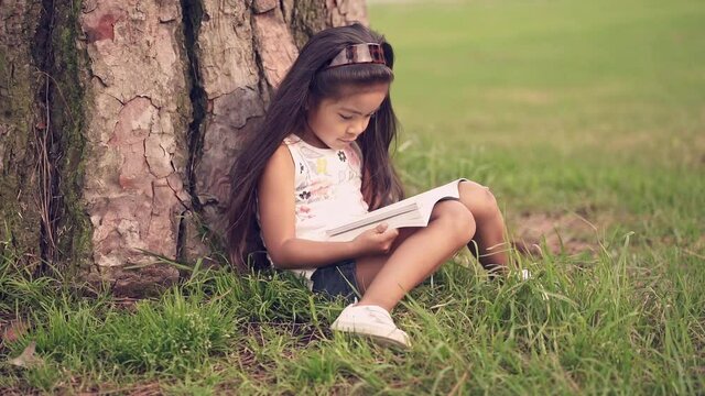 Young girl reading a book under a tree in the park