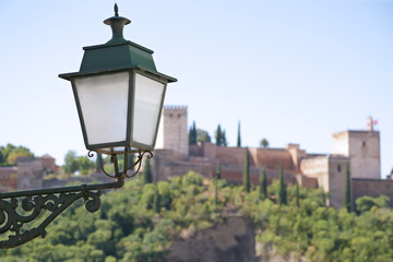 In the foreground a street lamp, in the background (out of focus) view of the Alhambra the ancient arabic fortress located in Granada, Spain