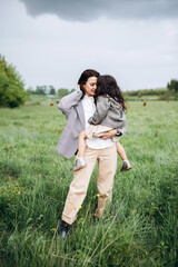 Naklejka na ściany i meble Stylish mother and daughter have fun outdoors in a field with green grass by the river when it rains