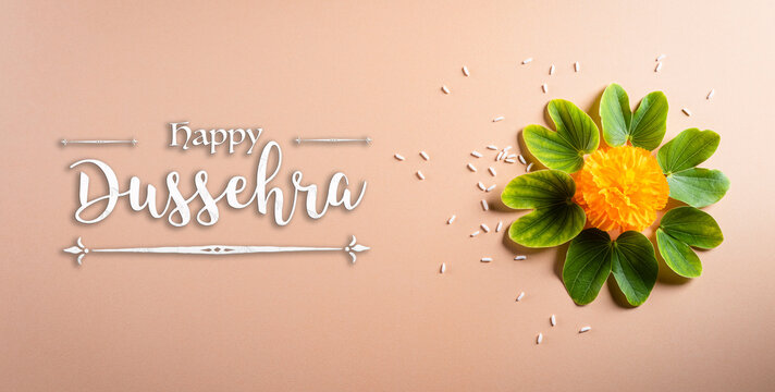 Happy Dussehra. Yellow flowers, green leaf and rice on orange pastel background. Dussehra Indian Festival concept.