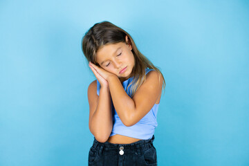 Young beautiful child girl over isolated blue background sleeping tired dreaming and posing with hands together while smiling with closed eyes.