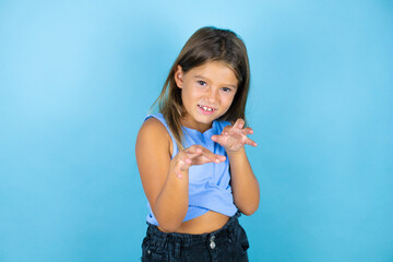 Young beautiful child girl over isolated blue background smiling funny doing claw gesture as cat, aggressive and sexy expression