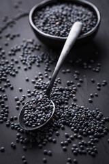 Beluga lentils on black background. Black lentils in bowl with spoon.