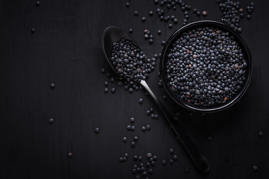 Beluga lentils on black background. Black lentils in bowl with spoon.