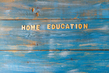 inscription home education is made of small wooden blocks printed on a wooden blue background with copy space. Layout, top view
