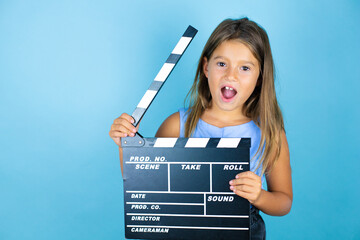 Young beautiful child girl over isolated blue background holding clapperboard very happy having fun
