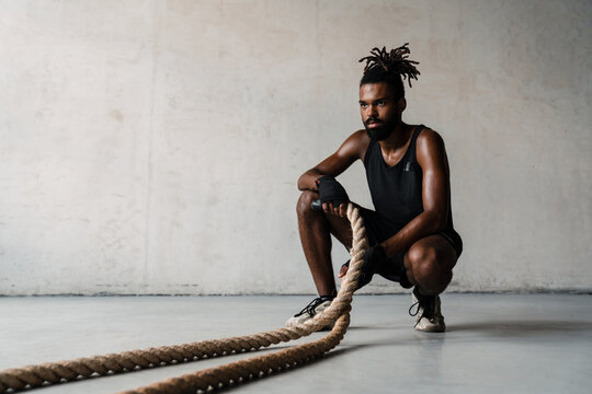Image of african american sportsman working out with battle ropes