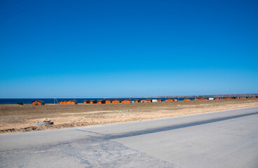 Bright orange bungalows stand in the steppe next to the sea. A Sunny summer day with a cloudless sky.