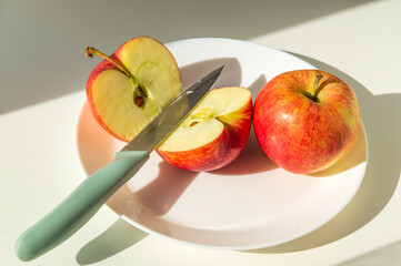 Ripe red apples in a plate with knife in the sunlight. Cut an Apple before eating to follow diet