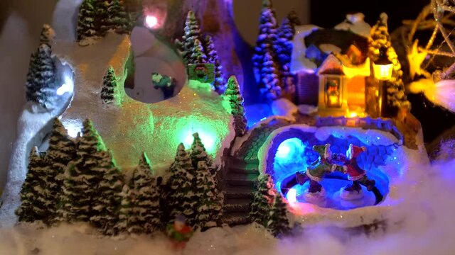 Motion miniature figurine Skiers couple ice skating and kids sleding in Christmas toy village snow set. 
