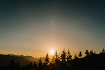 Silhouette of mountains at sunset or sunrise. Trees and forest on a background of the sun.