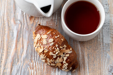 Croissant with almond flakes on wooden background, french breakfast in a cafe