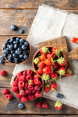 Berries. Various berries in wooden bowls on a brown wooden table. Strawberries, raspberries and blueberries in bowls